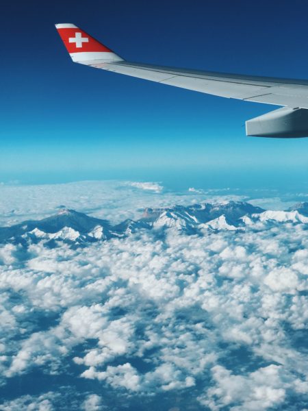 Symbolbild: Blick aus dem Fenster eines Flugzeuges. Schweizerflagge auf dem Flügel.